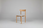 Wooden chair with a white cushion on a green wall and wooden floor.